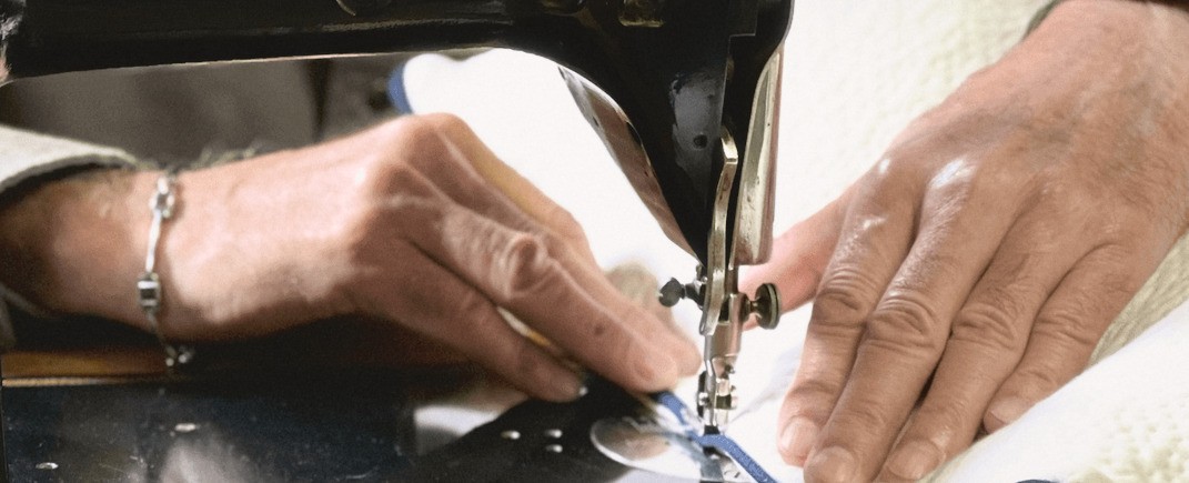 Two hands guiding quilted white cotton under the needle of a black Bernina sewing machine.