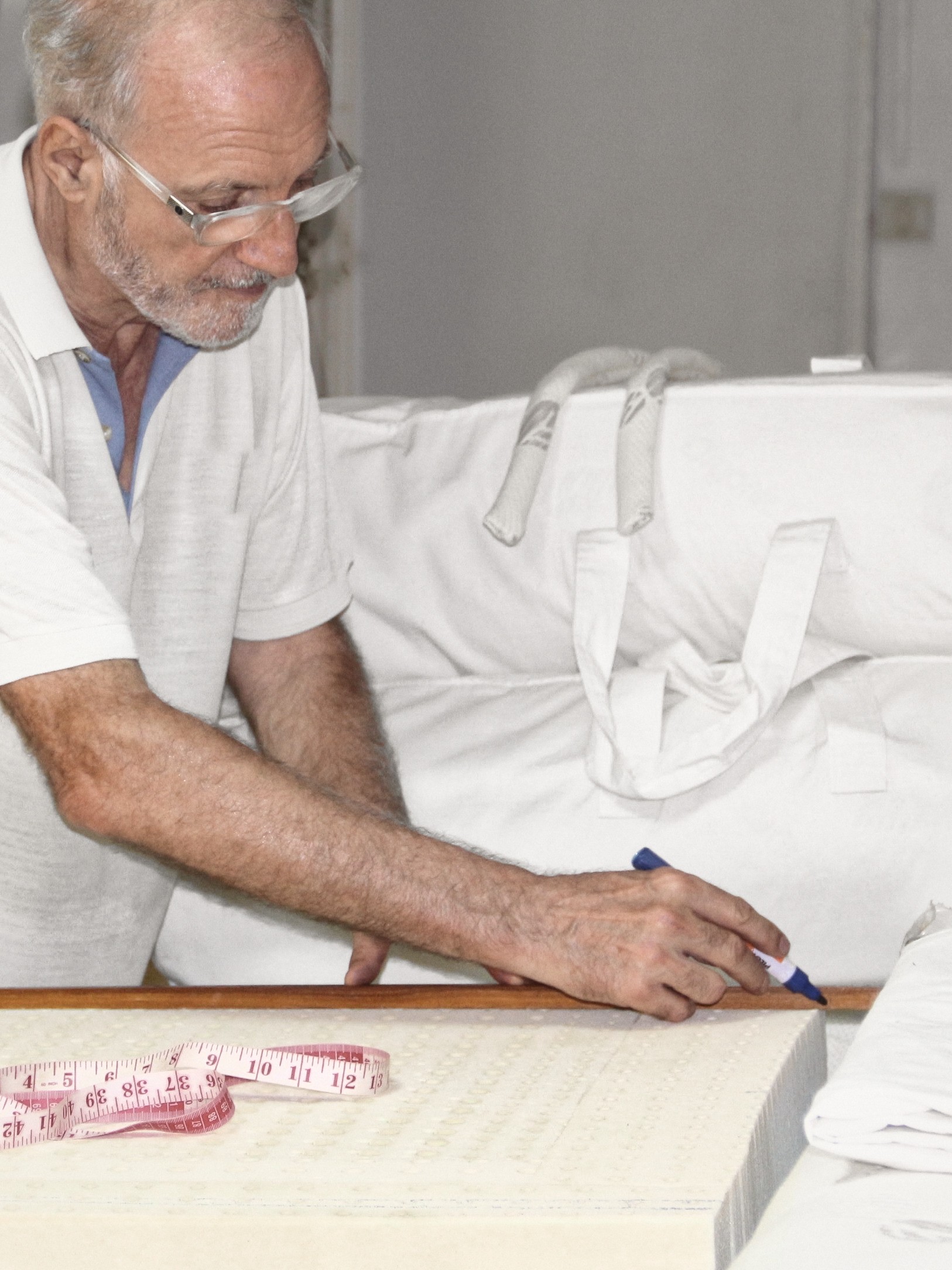 Dominique Bienfait in a white polo and glasses, leaning over a block of latex and drawing a line with a marker along a wooden rule, a tape measure in front of him.