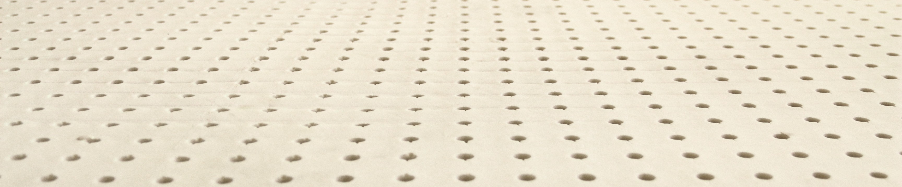 Close view across a sheet of natural latex, rows of round pin holes running away from the camera.