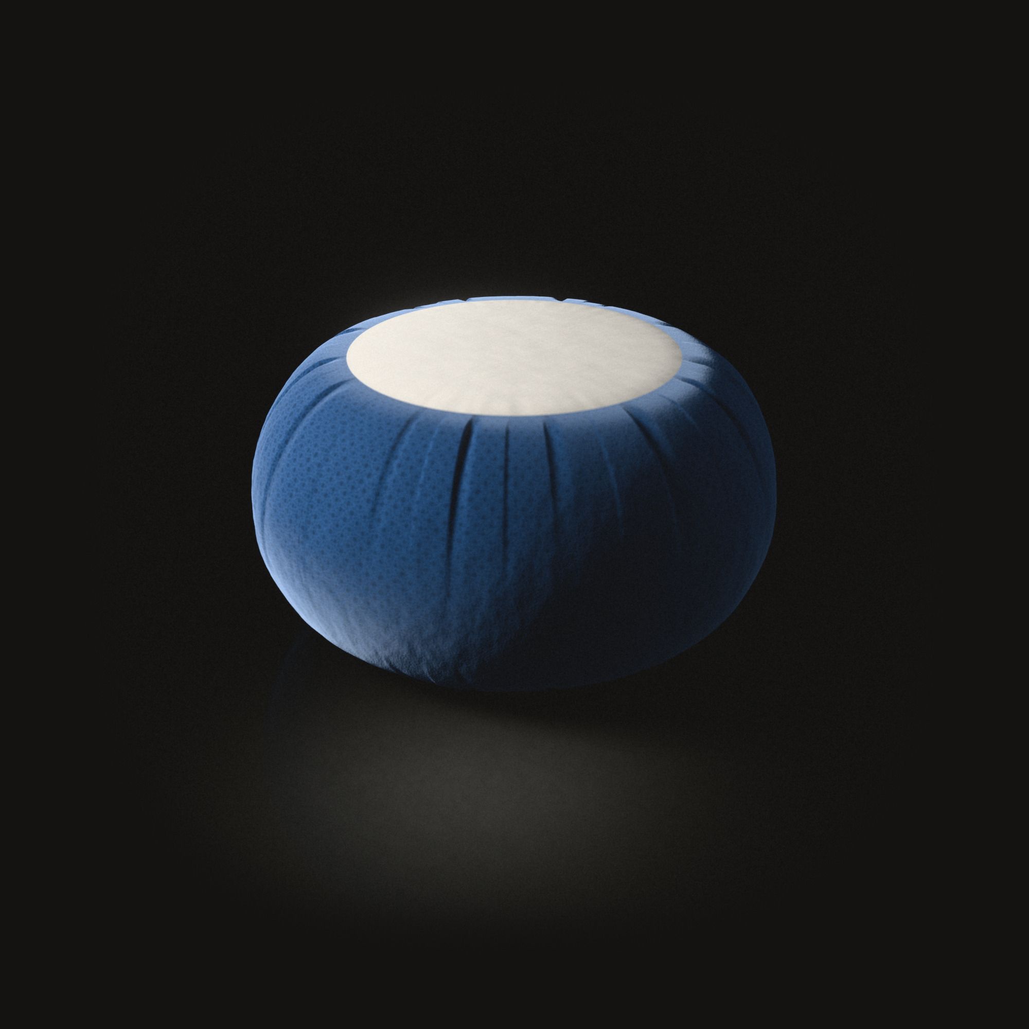 Un coussin de méditation rond et bleu sur un sol noir, le flanc plissé, un disque plat de coton crème sur le dessus.