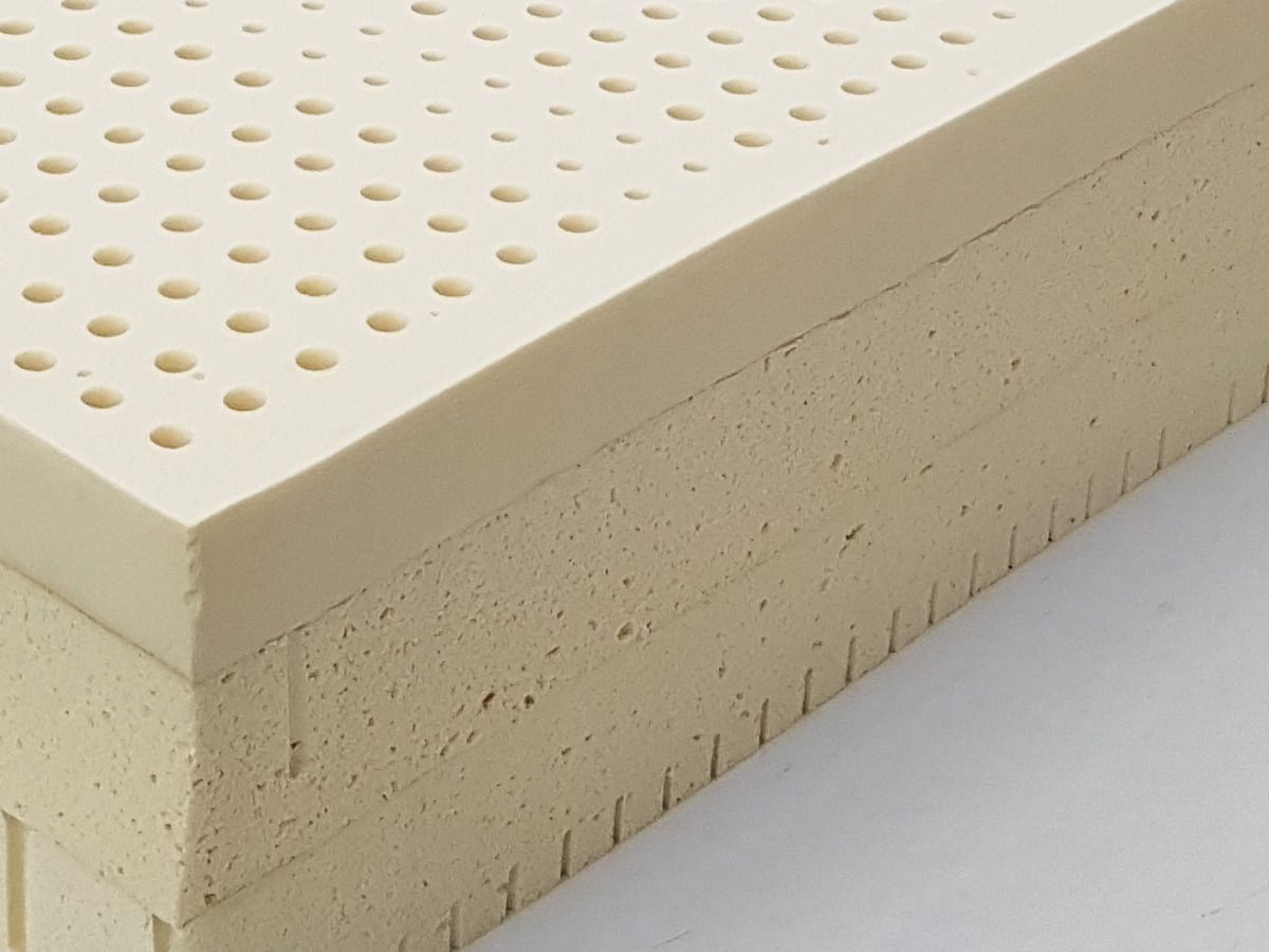 The corner of a stack of natural latex layers seen close: pin holes on top, the cut edge below.